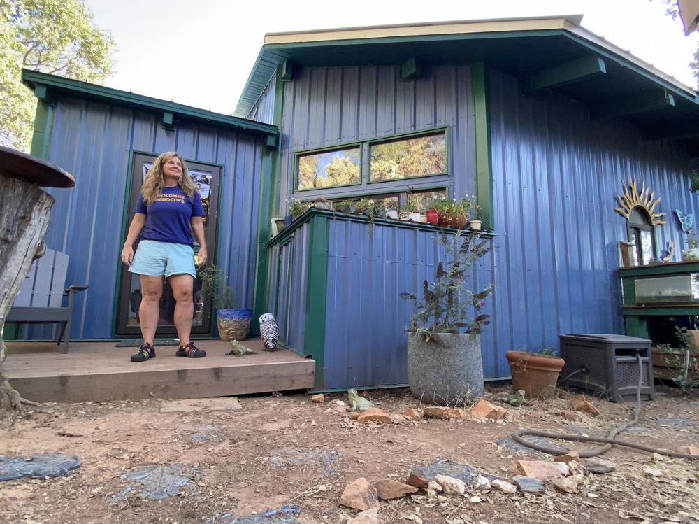 Beth Pratt stands outside her home near Yosemite National Park. Pratt added a metal roof, traded wood decking for laminate, installed a water tank and a fire hose, and cleared vegetation near the house to make it fire resistant. Despite this, her insurance carrier dropped her because of wildfire risk.