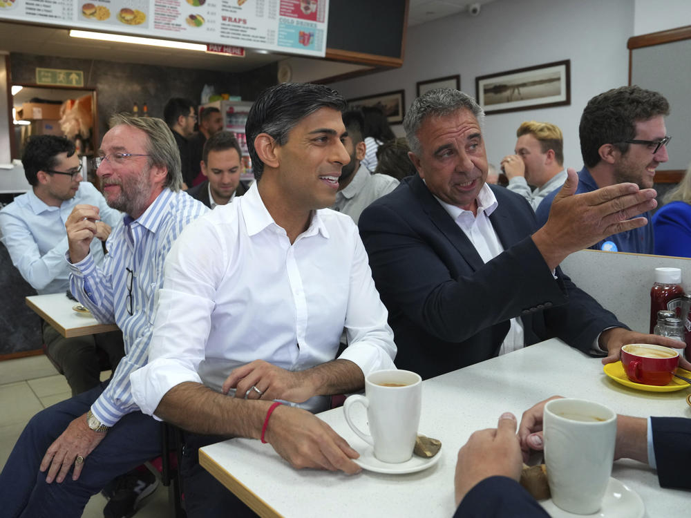Britain's Prime Minister Rishi Sunak, center, and newly elected Conservative MP Steve Tuckwell, center right, speak at the Rumbling Tum cafe in Uxbridge, after Tuckwell won the Uxbridge and South Ruislip by-election, west London, Friday July 21, 2023.