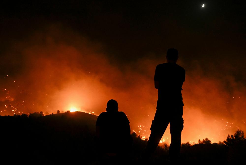 July 23, 2023: People watch the fires near the village of Malona in the Greek island of Rhodes.
