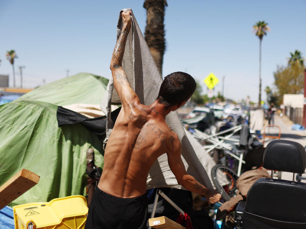 A homeless person adjusts a friend's tent to help increase shade cover in a section of The Zone, Phoenix's largest homeless encampment.