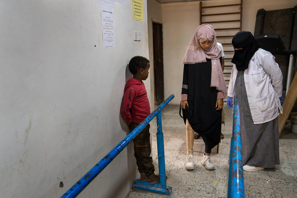 Shaimaa Ali Ahmed begins her physical therapy at the encouragement of her doctor (right). Her gait is uneven, but she moves quickly along the parallel bars.