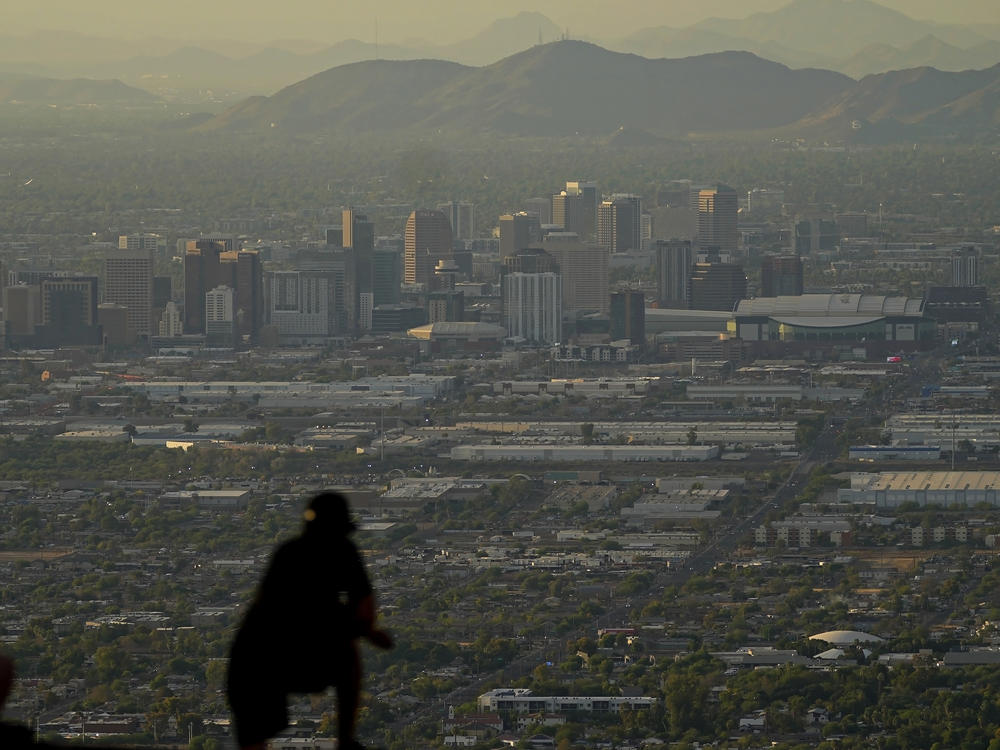 A man overlooks downtown Phoenix at sunset atop South Mountain, Sunday, July 30, 2023. Some slight relief may be on the way as seasonal thunderstorms could drop temperatures in Phoenix on Monday and Tuesday. (AP Photo/Matt York)