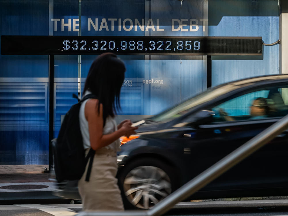 Pedestrians walk past a poster and electronic billboard about the national debt displayed ain  street in Washington, D.C., on July 5, 2023. The U.S. last had a budget surplus in 2001. Since then it's seen its deficits surge.