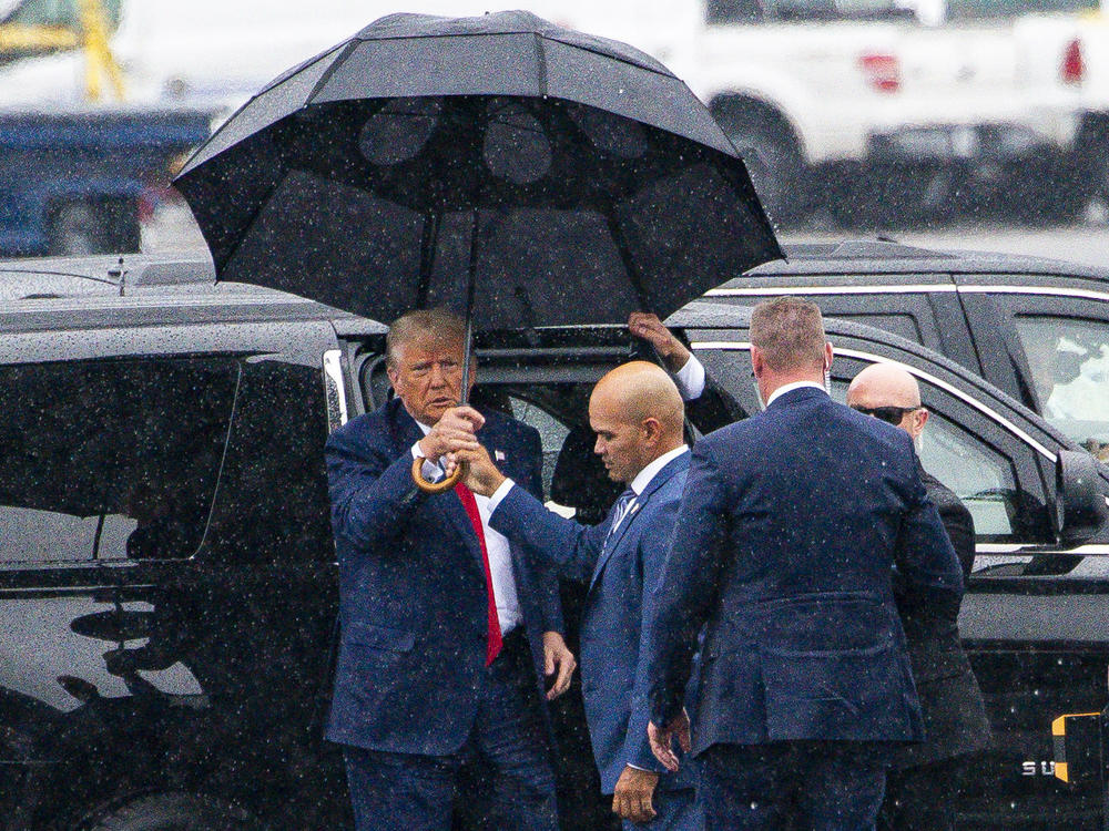 Donald Trump, left, is handed an umbrella from Walt Nauta, his personal aide and co-defendant in a felony case in Florida, on Thursday, the day the former president pleaded not guilty to four felony charges in Washington, D.C.