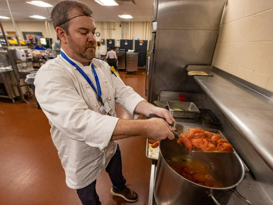 Michael Hawley, general manager of the kitchen at Faulkner Hospital, places roasted tomatoes into a pot as he prepares the roasted tomato and shallot coulis.