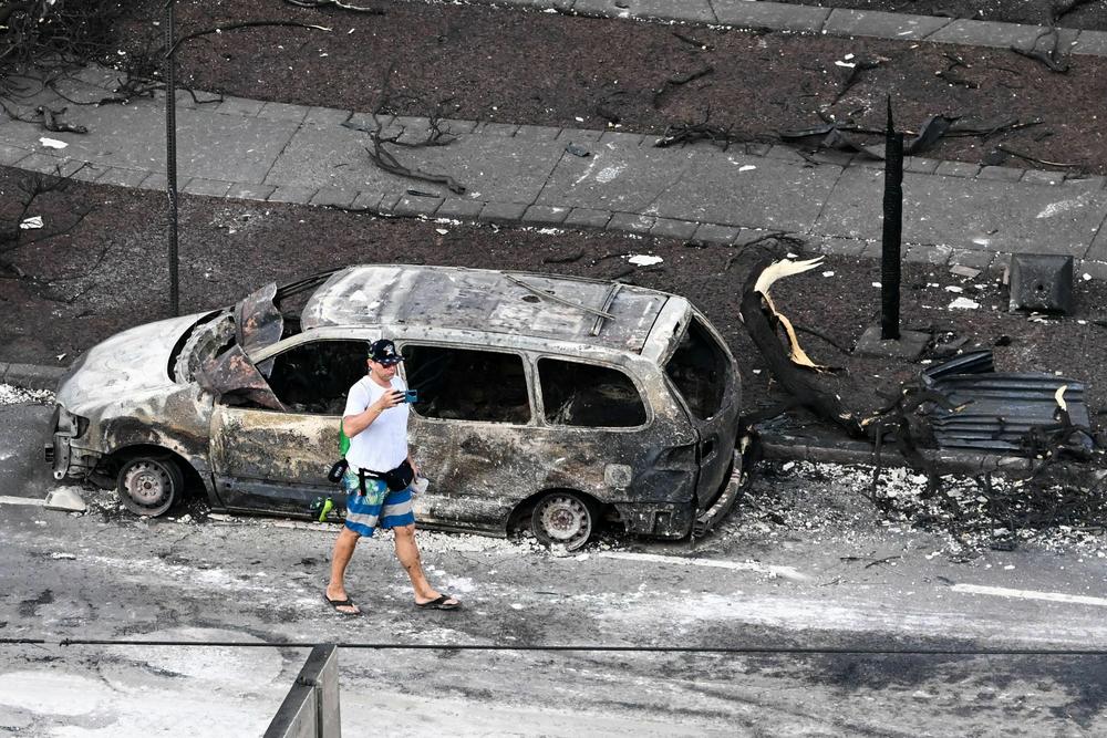August 10: A person walks past a destroyed car in the aftermath of wildfires in western Maui in Lahaina, Hawaii.