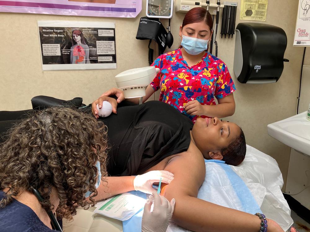 Nurse practitioner Arin Kramer prepares to insert a contraceptive implant under the skin of I'laysia Vital's upper arm, as physician assistant Andrea Marquez (rear) offers support. Vital will attend college at Texas Southern University in Houston, where most abortions are banned.