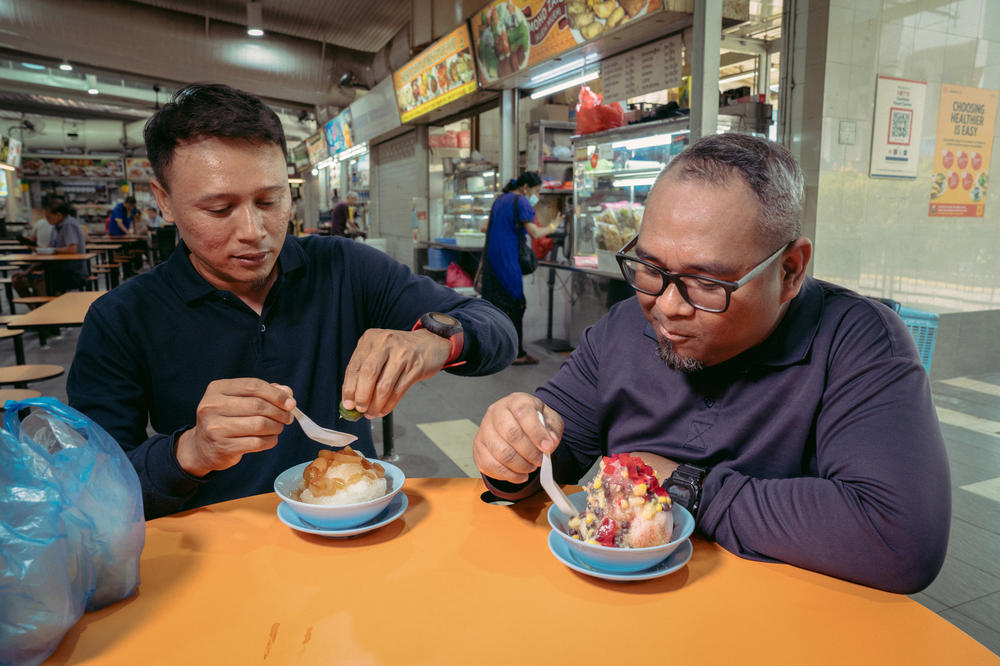 Muhammad Azreen (left) and Airul Hizen (right) enjoy sea coconut ice jelly and ice kachang from Jin Jin dessert at ABC Brickworks Market & Food Center. When bought at one of the large food courts in the country, called hawker centers, the dessert is  generally an affordable way to cool down at 2 - 4 SGD ($1.48 to $2.96).