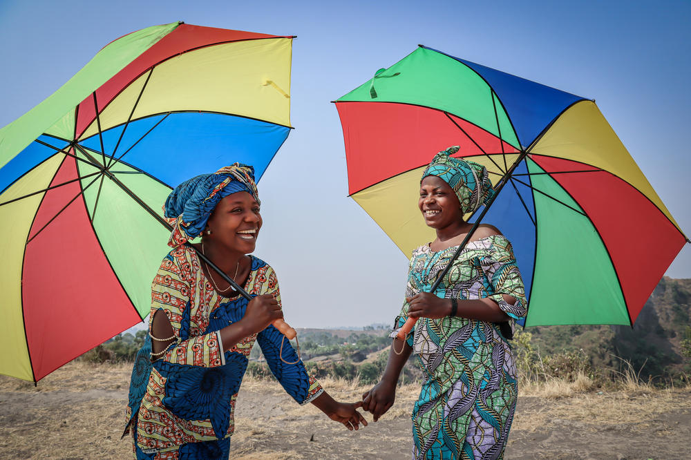 Néema Byanyira (left) chats with Ange Furaha under the shade of their umbrellas. Byanyira says one reason she uses one is to keep her makeup from running.