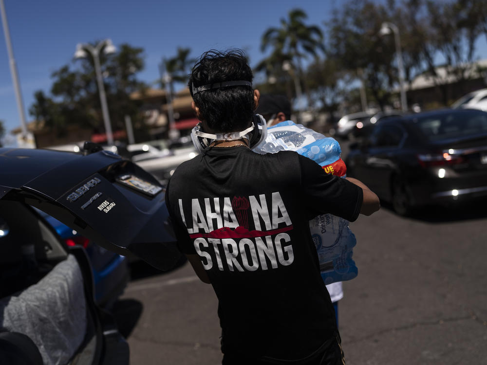 Ken Alba, a Lahaina, Hawaii, resident, carries a bag of ice at a food and supply distribution center set up in the parking lot of a shopping mall in Lahaina, Hawaii, Thursday, Aug. 17, 2023. The blazes incinerated the historic island community of Lahaina and killed more than 100 people.