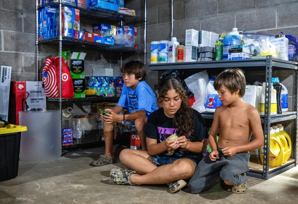 Caleb, 11, Bella, 12, and Nash Cabanilla Okano, 8, sit in a supply room at the house where they're taking shelter after their homes were destroyed.