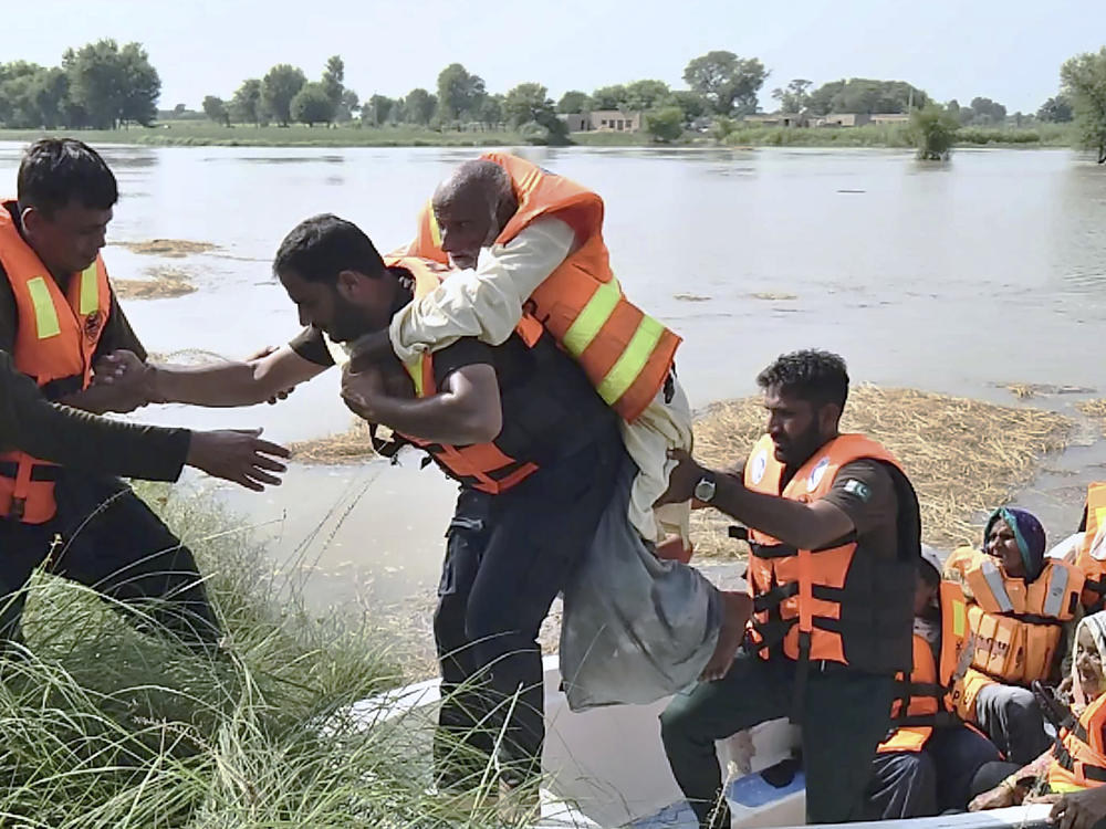 In this photo released by Rescue 1122 Emergency Department, rescue workers help a villager as he and others are being evacuate from a flooded area of Bahawalnagar district in Pakistan's Punjab province on Wednesday, Aug. 23, 2023.