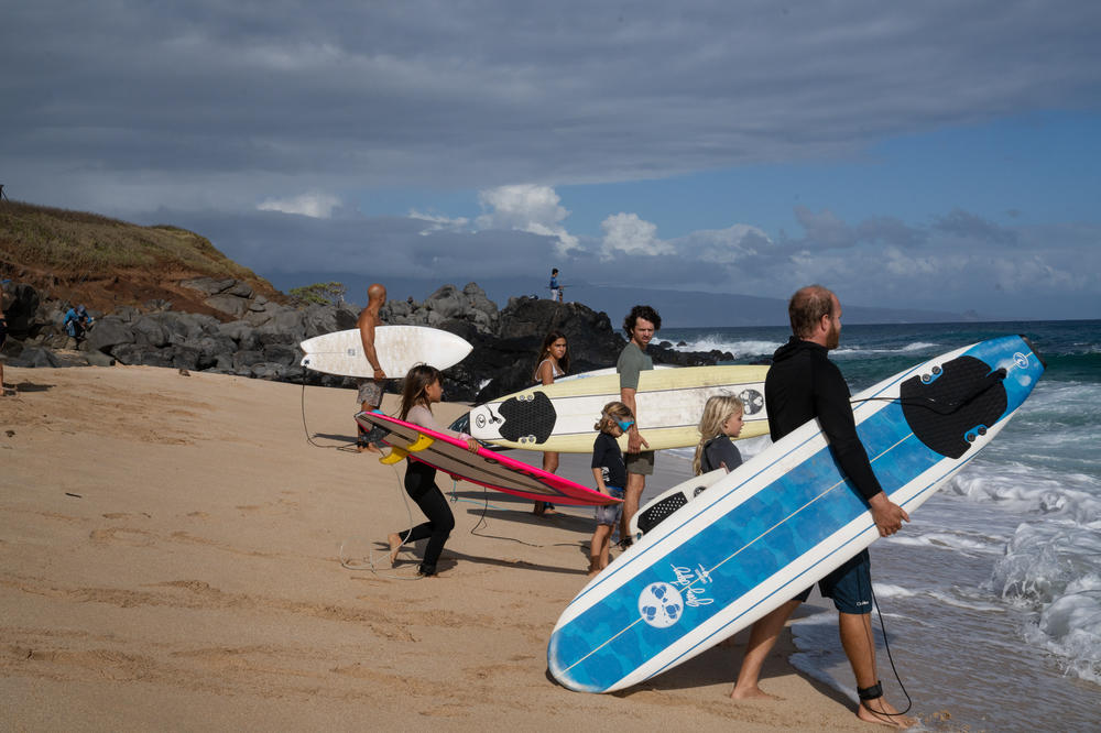 A group of kids and adults approaches the water to begin surfing.