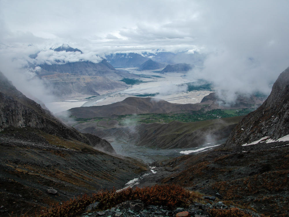 A view of the Pakistani territory of Baltistan from the heights of the mountain above the village of Chunda. The patches of white in the foreground are snow and water. The patches of silver in the distance are clouds that shroud the peaks of most mountains in Baltistan. The territory boasts towering peaks, including K2, the world's second highest mountain.