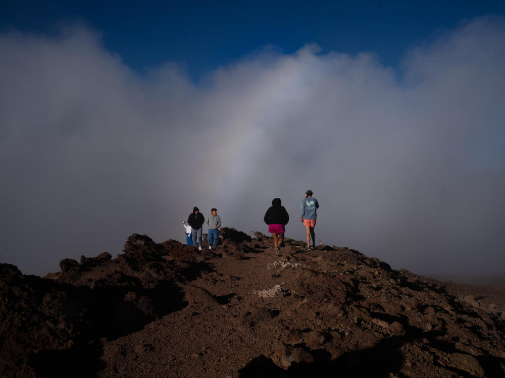 A few tourists stand under a rainbow as the clouds clear at Haleakalā on the island of Maui, Hawaii. Though much of the island is untouched, tourism is down drastically.