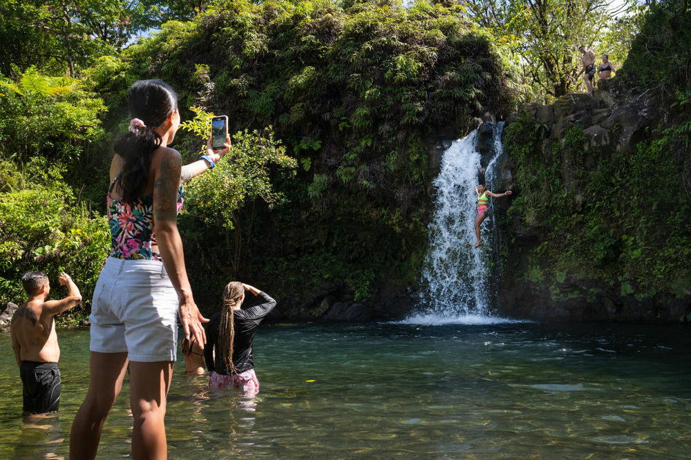 Tourists jump into a pool of water next to a waterfall at Pua'a Ka'a State Wayside Park.