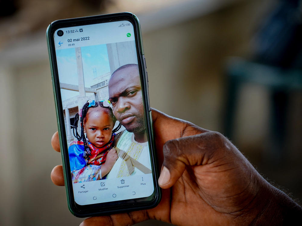 Wuri Bailo Keita, 33, holds a mobile phone showing a picture of himself and his late daughter, Fatoumatta, who is believed to have died of acute kidney failure after ingesting contaminated cough syrup manufactured in India. The family lives in Banjul in The Gambia. The photo is from October 10, 2022.