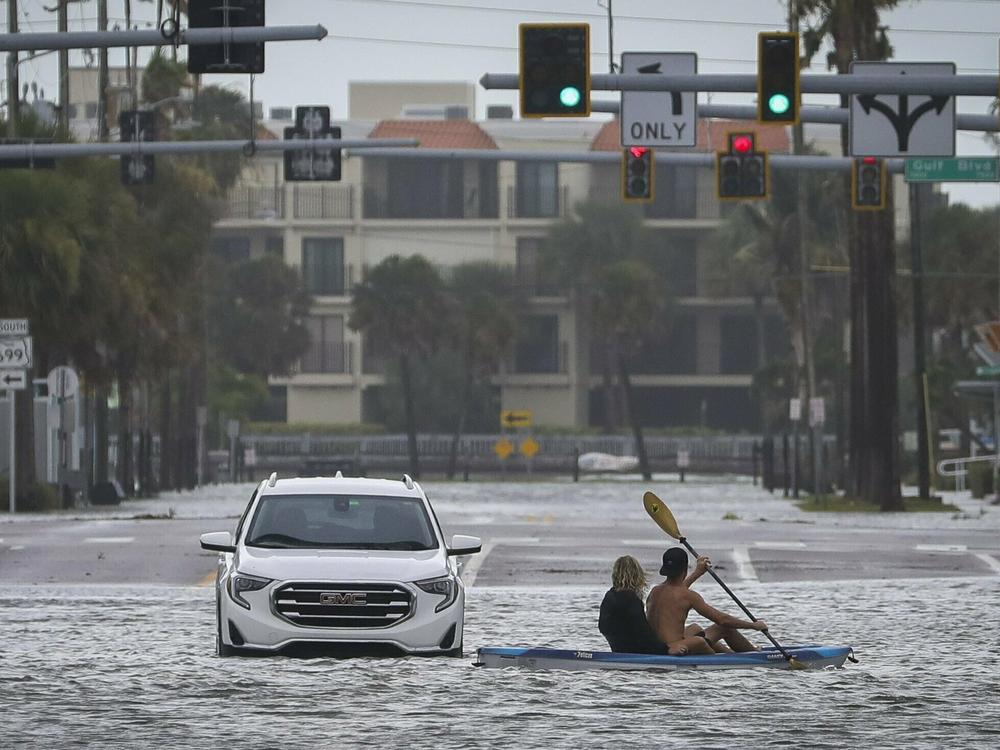 People kayak past an abandon vehicle in the intersection of Boca Ciega Drive and Pasadena Avenue Wednesday, Aug. 30, 2023 in St. Pete Beach, Fla.