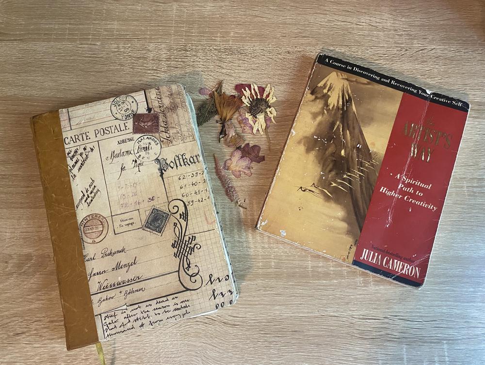 The author's well-loved copy of <em>The Artist's Way</em>, with a journal and some flowers she gathered during an artist date.