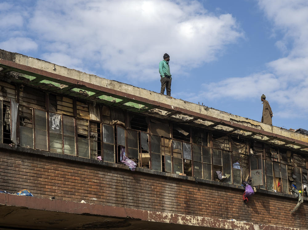 Squatters stand on a rooftop overlooking the scene of one of South Africa's deadliest inner-city fires in Johannesburg, South Africa, Friday.