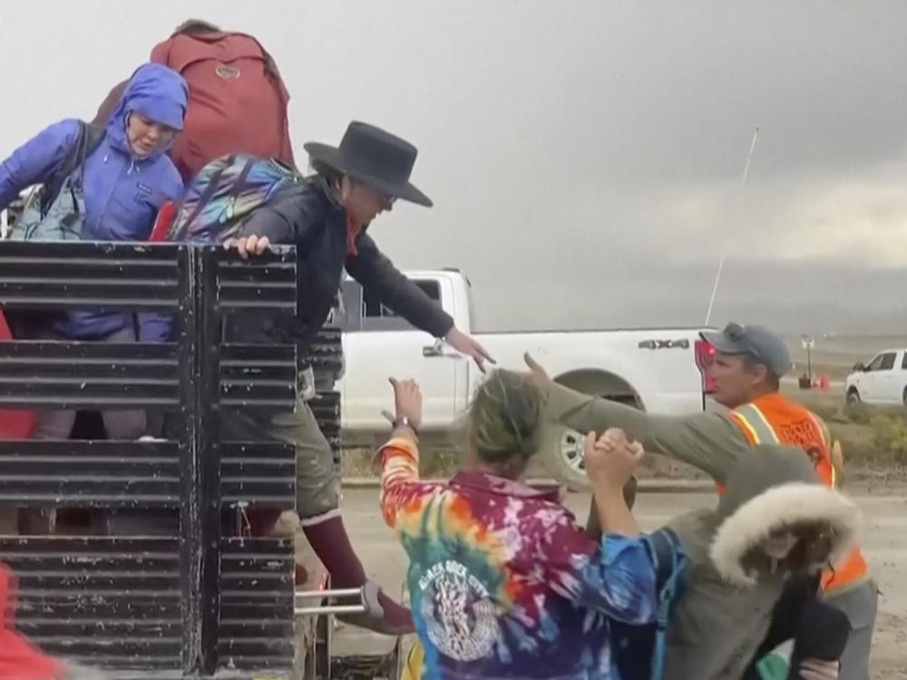 In this image from video provided by Rebecca Barger, festival-goers are helped off a truck from the Burning Man festival site in Black Rock, Nev., on Monday, Sept. 4, 2023.
