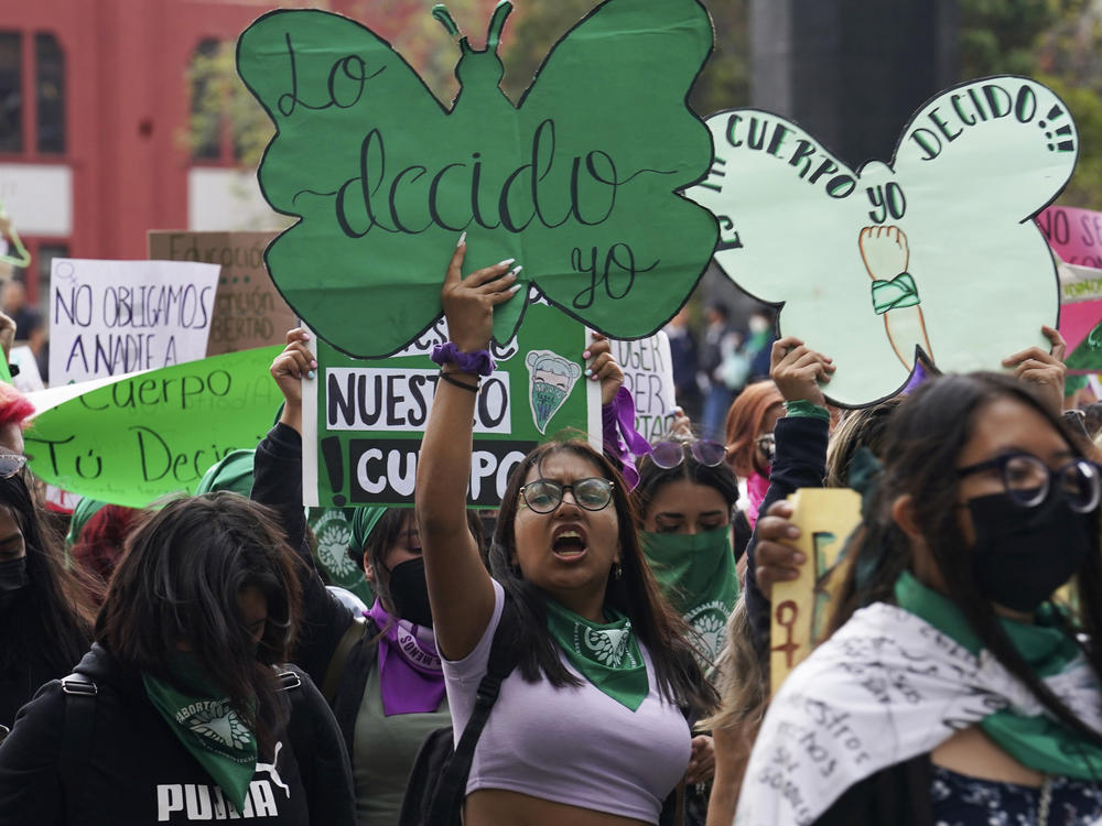 A woman holds up a sign with a message that reads in Spanish; 