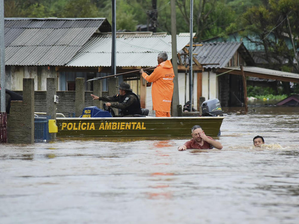 Police officers check a house as residents wade through a flooded street after floods caused by a cyclone in Passo Fundo, Rio Grande do Sul state, Brazil, Monday.