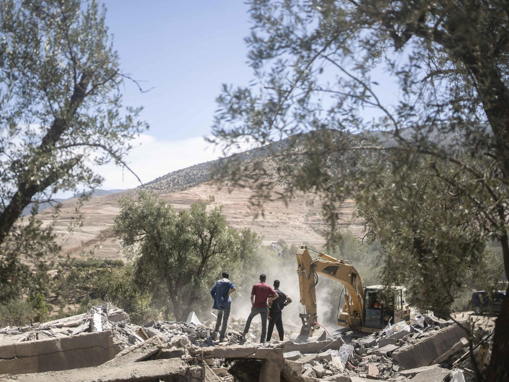 People watch as a tractor removes rubble caused by the earthquake in the village of Tafeghaghte. Rescue crews expanded their efforts on Monday as the earthquake's death toll continued to climb to more than 2,400.