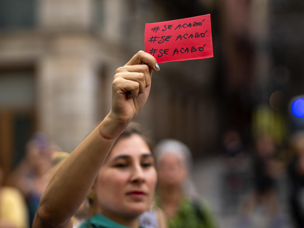 A demonstrator holds a red card reading in Spanish 