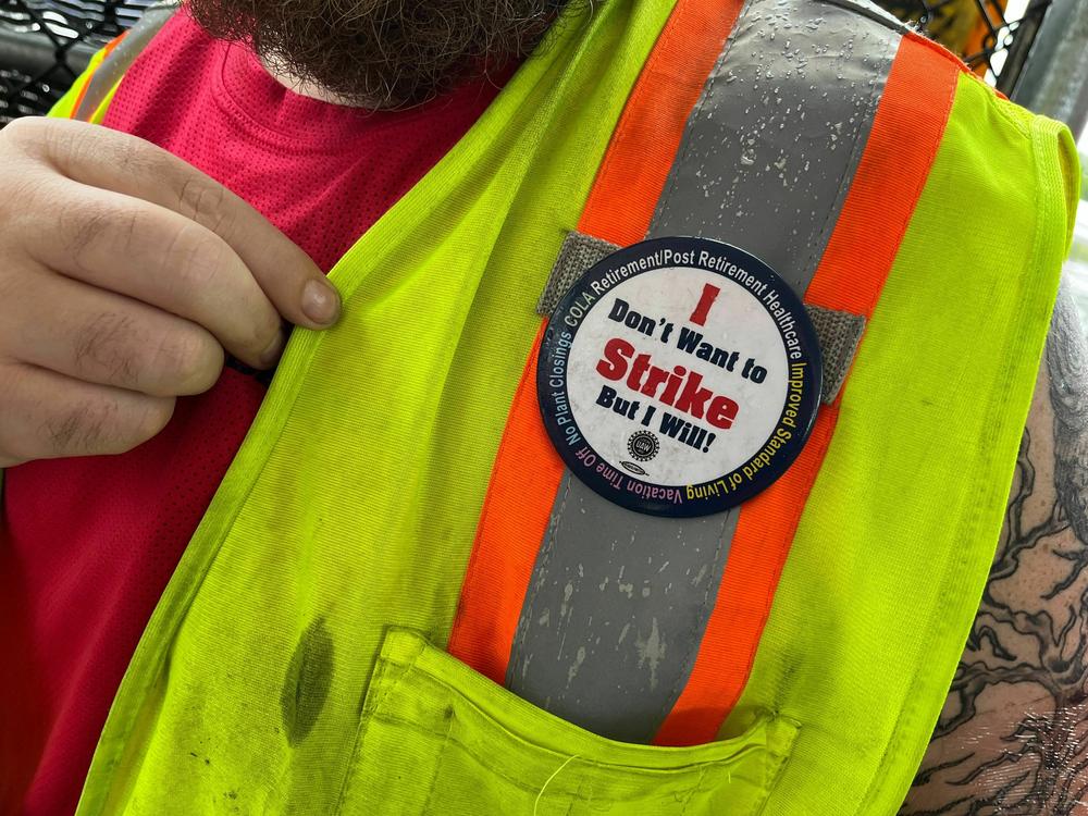 An autoworker outside the Ford Michigan Truck plant shows a pin on his fluorescent yellow and orange vest reading 