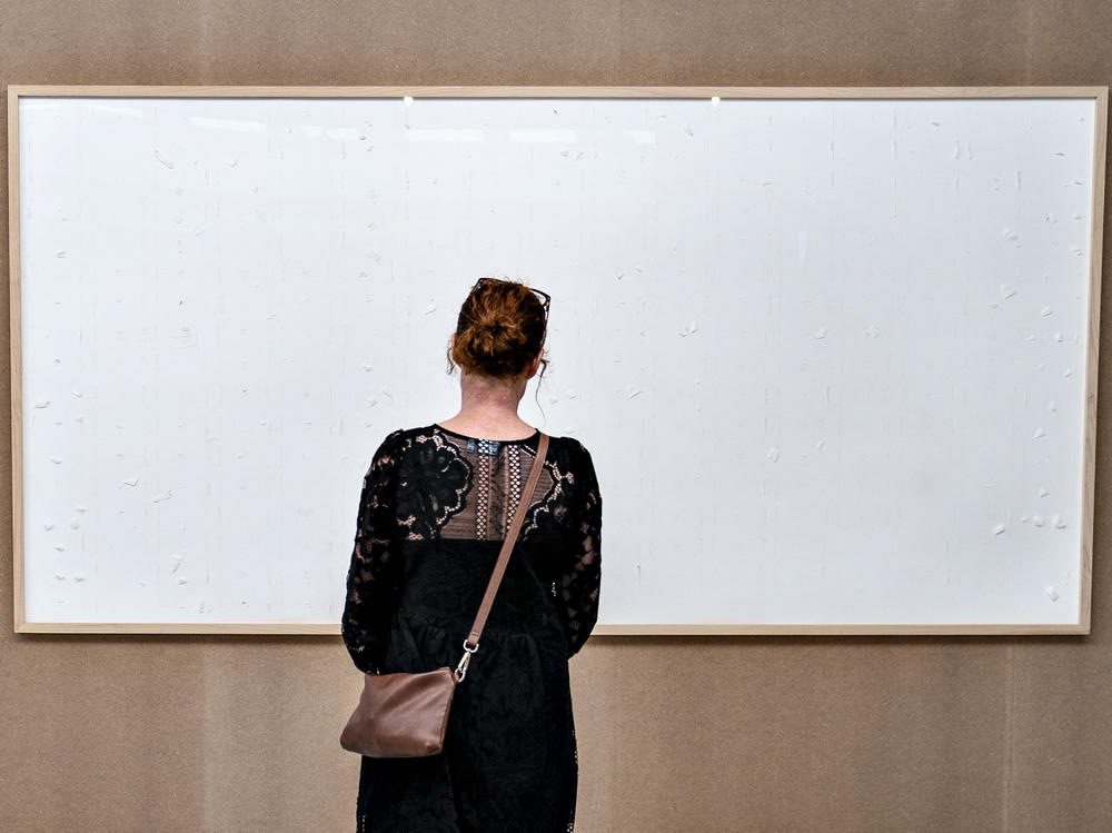 A woman stands in front of an blank canvas hung up at the Kunsten Museum in Aalborg, Denmark, in 2021. Danish artist Jens Haaning sent the museum blank canvasses under the title <em>Take the Money and Run</em>.