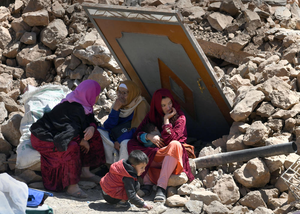 Amid debris, Aicha Ounasser sits with neighbors under a damaged door in Tnirte on Sept. 12.