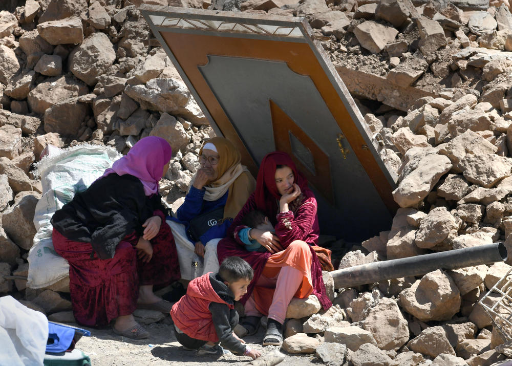 Amid debris, Aicha Ounasser sits with neighbors under a damaged door in Tnirte on Sept. 12.