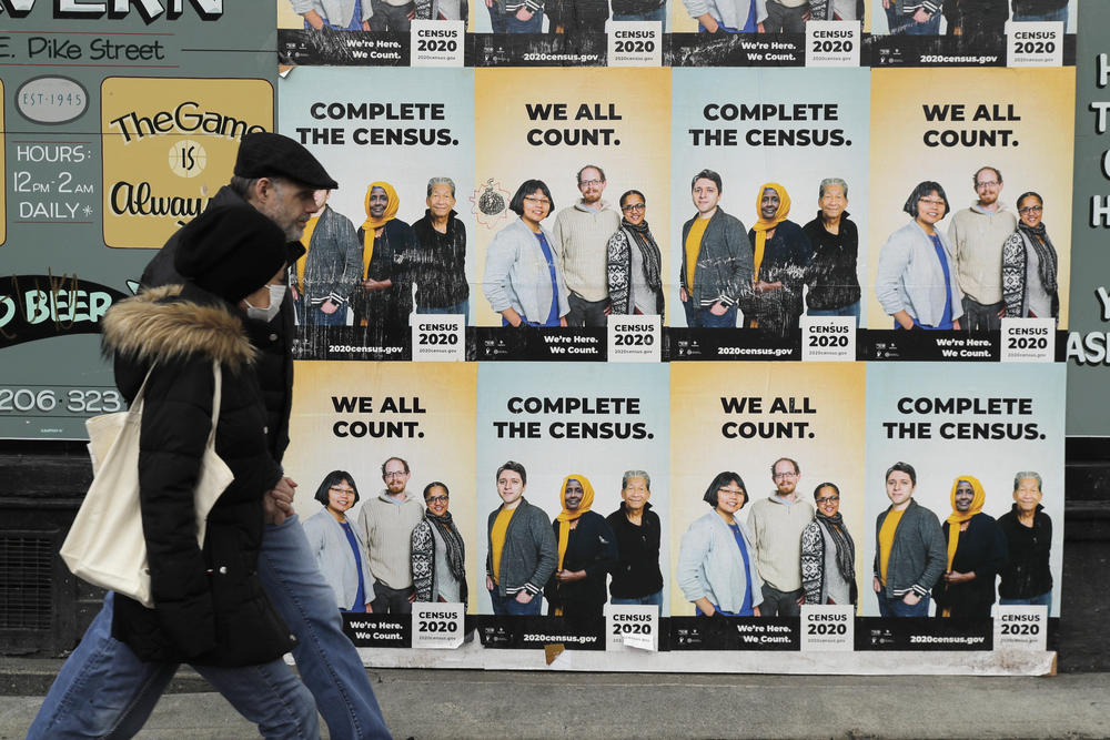 People walk past posters encouraging census participation in Seattle in 2020.
