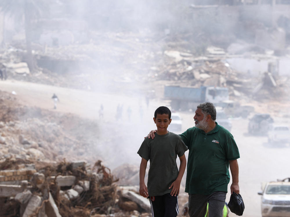 A father walks with his son in Derna, Libya, with smoke caused by a sanitation truck visible in the background. Concerns are rising about the spread of infectious diseases after fatal floods in Derna earlier this month.