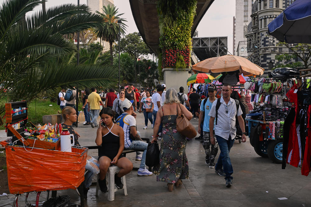 People walk by vendors in a plaza in the afternoon in downtown Medellín.