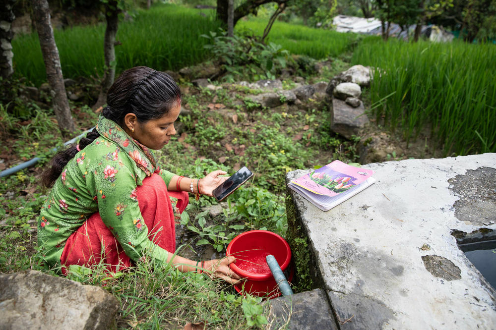 Kiran Joshi places her bucket under flowing water and times the duration with her phone. She stops the timer once the bucket is full and repeats the measurement three times. The results will help determine if efforts to 