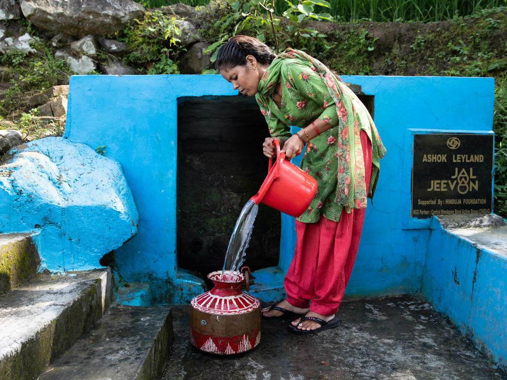 Kiran Joshi fills a copper vessel with water from Ashwanaula, a groundwater spring in the village of Raushil, where she lives with her family