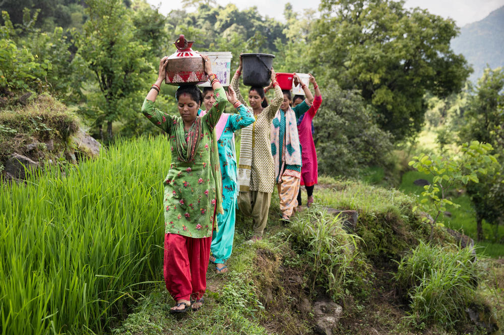 Members of Raushil village's water committee, lead by Kiran Joshi, carry pots and buckets of water from Ashwanaula, a groundwater spring, to their respective homes.
