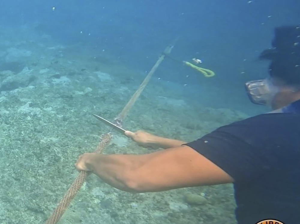 This photo, provided by the Philippine Coast Guard on Sept. 26th, shows a diver cutting rope tied to a floating barrier at the Scarborough Shoal in the South China Sea.