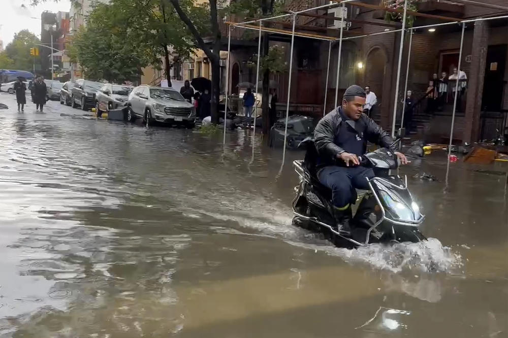 In this photo taken from video, a man drives a scooter through flood waters, Friday, Sept. 29, 2023, in the Brooklyn borough of New York.