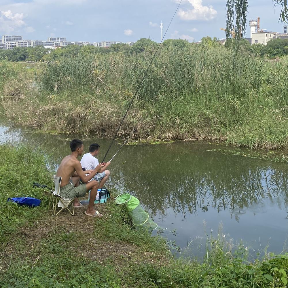 Li Tao and his buddy dabble lines in a slow-moving river channel in Jinhua, China, occasionally pulling out a tiny fish.