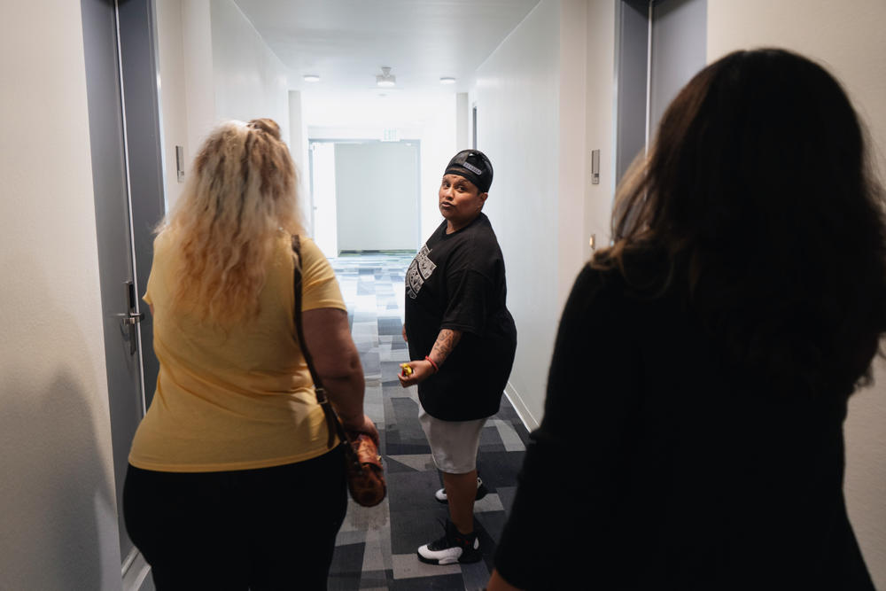 Valarie Zayas (left) and Dulce Volantin (center) walk down the hallway of their apartment building with case manager Hannia Centeno.
