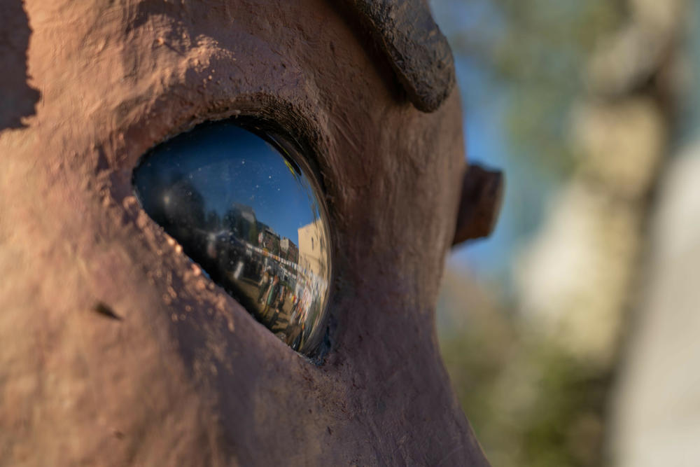 A crowd of people at The World's UnFair is reflected in the glass eye of the animatronic talking tree.