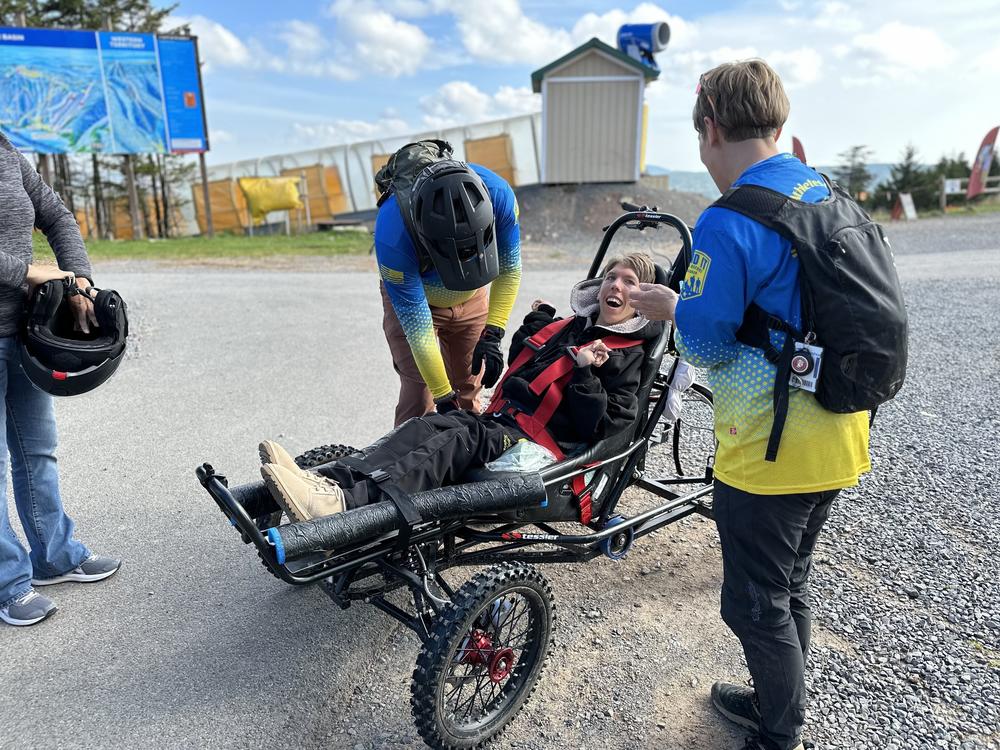 Before heading out on the trail, Carol Woody and volunteer Erwin Berry make sure Gage Tatar is safely buckled into the Cimgo. Grinning wide, Tatar listens as Woody explains what he can expect on the dirt track.