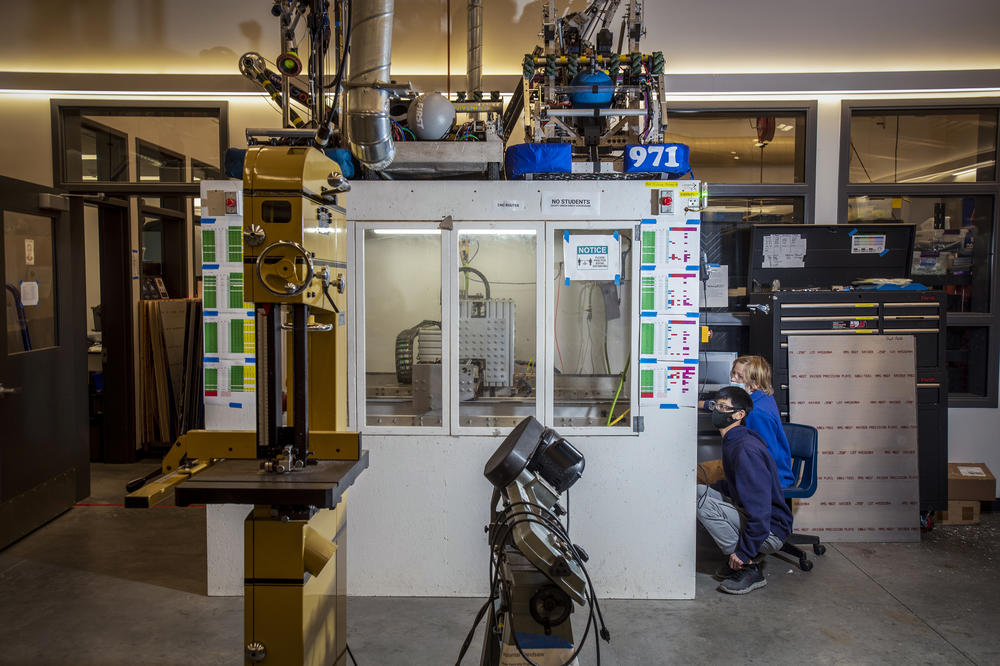 Sophomores Adriel Lim and Daniel Kessens monitor the progress of the CNC (computer numeric control) router in the Spartan Robotics machine shop, which also serves as a repository for Team 971's previous robots above.