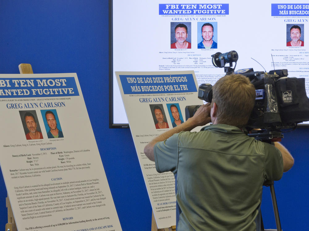 A television cameraman films the photographs of an alleged sexual predator, Greg Alyn Carlson, as he is listed on the FBI Ten Most Wanted fugitive list, during a news conference at the FBI office in Los Angeles on Sep. 27, 2018.