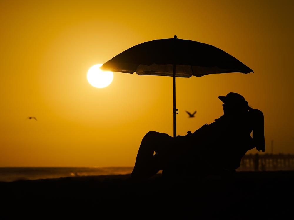 A person rests under an umbrella as the sun sets, Sept. 12, 2023, in Newport Beach, Calif. After a summer of record-smashing heat, warming somehow got even worse in September as Earth set a new mark for how far above normal temperatures were, the European climate agency reported.