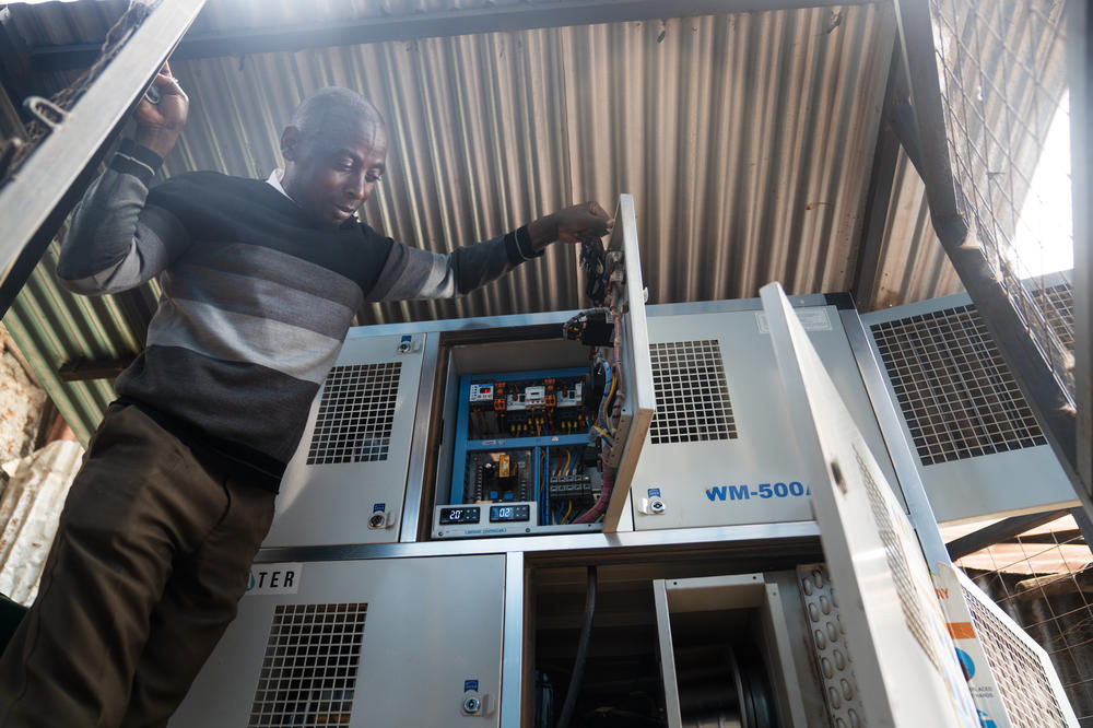 The teacher Musonye shows the air-to-water system that was installed at the school. It uses fans to suck in hot, moisture-filled air, and then cools the air to condense the water – much like a dehumidifier or an AC unit. The water is then filtered and minerals are added, making it safe for drinking.