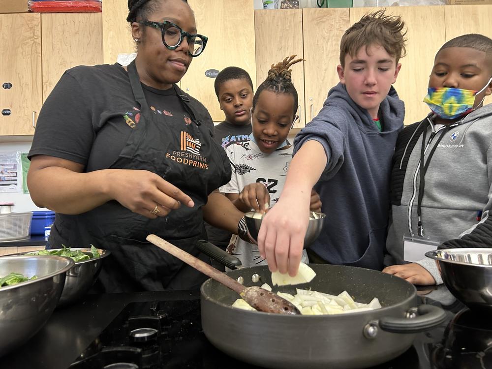 Students help instructional coach Regina Green caramelize onions for a dish featuring fresh greens from the school garden at Watkins Elementary.